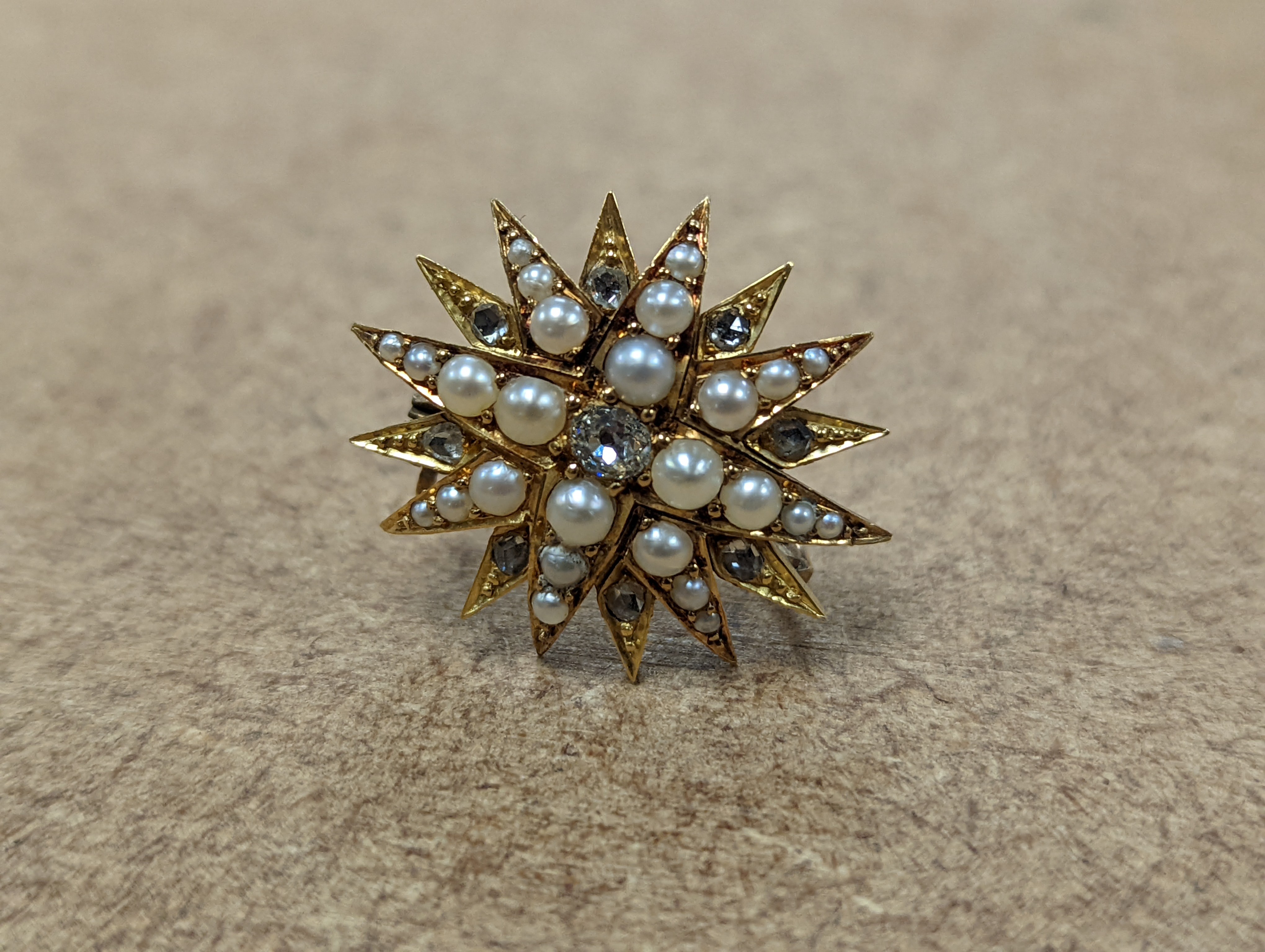 An Edwardian yellow metal, graduated split pearl and single stone diamond set starburst brooch(adapted?), 24mm, gross weight 6.5 grams.
